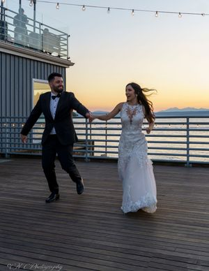 Couple dancing playfully on a seaside deck during sunset with string lights overhead.