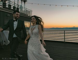 A sunset wedding ceremony on a waterfront deck with string lights overhead.