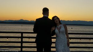 Silhouetted couple embraces against a dramatic sunset over the ocean with mountains in the background.