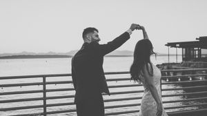 Black and white silhouettes of a couple posing dramatically on a seaside boardwalk.