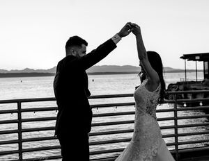 Silhouettes of a couple dancing on a waterfront pier during sunset.