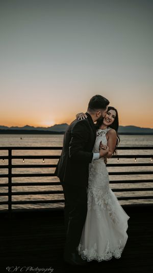 A romantic sunset silhouette series of a couple embracing on a waterfront pier with mountains in the background.