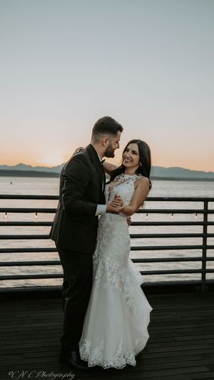 Romantic sunset wedding photos captured on a pier with mountains and water in the background.