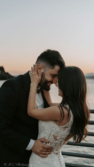 Intimate wedding couple embraces on wooden pier during golden hour with water views.