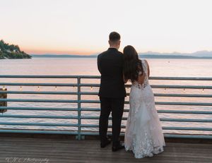 Silhouetted figures watching sunset from wooden pier with mountains in background.