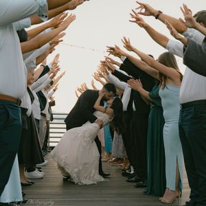 Wedding guests forming tunnel with raised arms on waterfront deck.