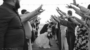 Wedding guests form a tunnel with raised arms as newlyweds dance beneath during a black and white reception celebration.