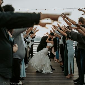 Wedding guests create celebratory archway on wooden deck for newlyweds to pass through.