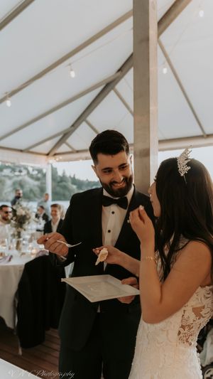 A couple shares a joyful moment while feeding each other cake during their wedding reception under a white tent.
