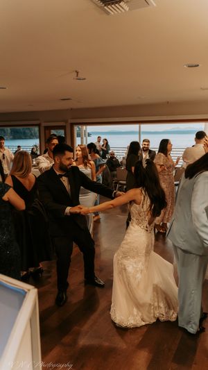 Wedding guests dancing together at an indoor reception with warm lighting and wooden floors.