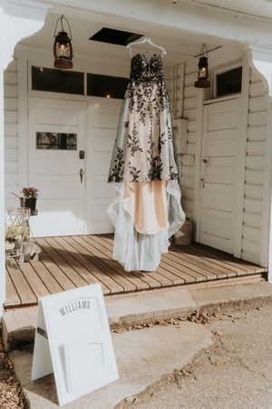 White wedding dresses and formal attire hang on display along a rustic wooden porch with white siding.
