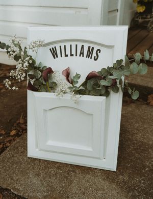 A series of white decorative cabinet doors with greenery arranged on top and the name 'Williams' visible on one panel.