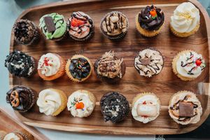Assorted gourmet cupcakes with colorful frosting and toppings displayed on a rustic wooden serving board.
