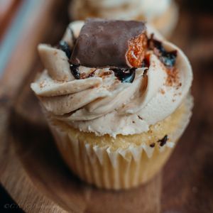 Homemade vanilla cupcake topped with whipped cream and chocolate shavings on a rustic wooden surface.