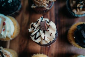Chocolate cupcake topped with vanilla frosting, chocolate drizzle and a chocolate piece on a dark wooden surface.