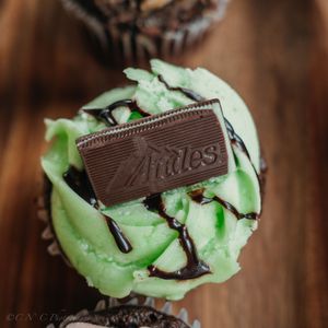 Close up view of mint chocolate chip ice cream scoops topped with chocolate pieces and drizzle on dark wooden surface.