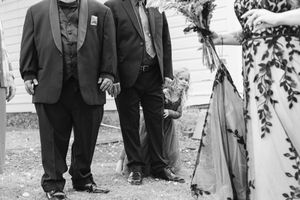 A black and white photograph shows people in formal attire walking outdoors in what appears to be a wedding procession.