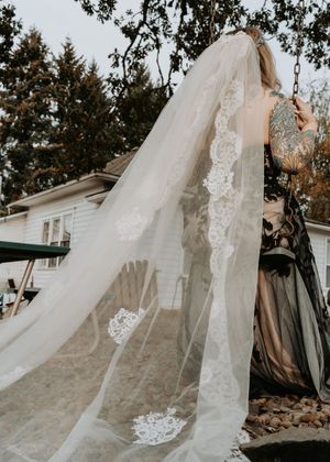 A flowing white wedding veil with lace details billows gracefully in the breeze against a natural outdoor backdrop.