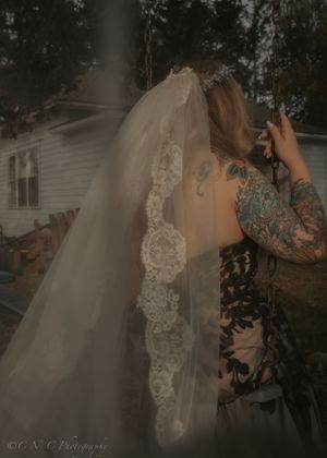 An ethereal bridal portrait shows a delicate lace-trimmed veil against a moody outdoor backdrop.