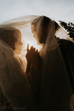 A romantic silhouette of a couple under a flowing veil backlit by golden sunlight.