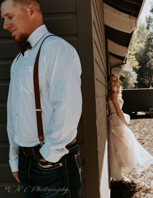 A stylish groom in suspenders and dress shirt stands in profile during a first look wedding moment.