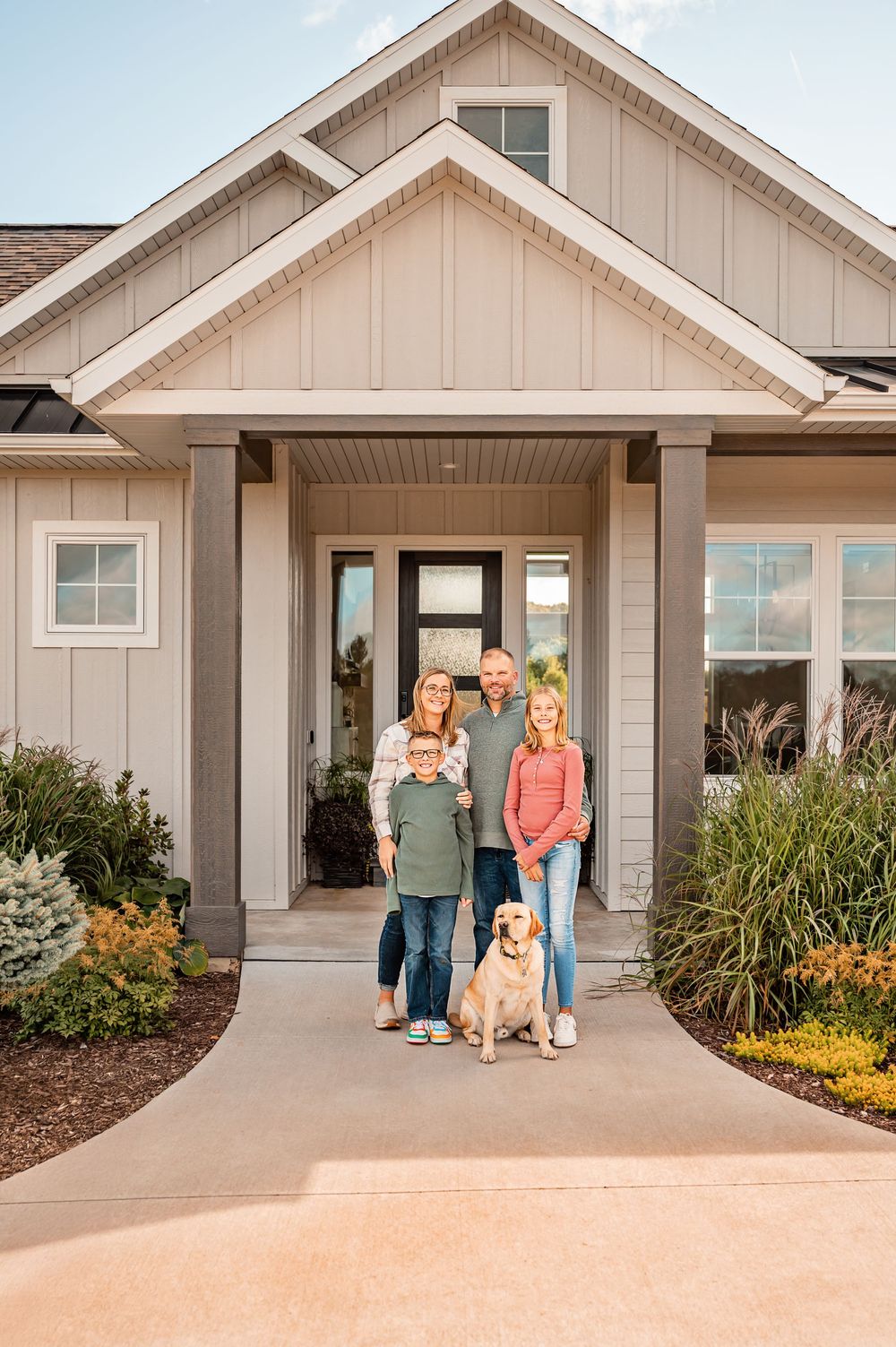 Modern craftsman style home exterior with white siding, tan trim, and landscaped mulch beds.