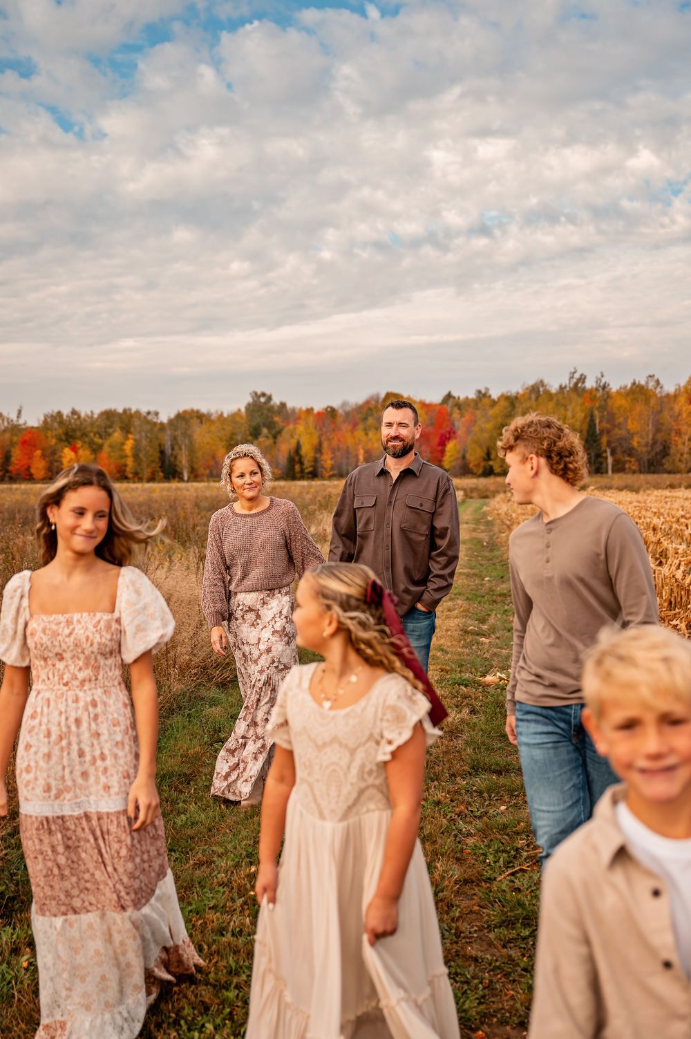A group stands together in a field during autumn with fall foliage and cloudy skies in the background.