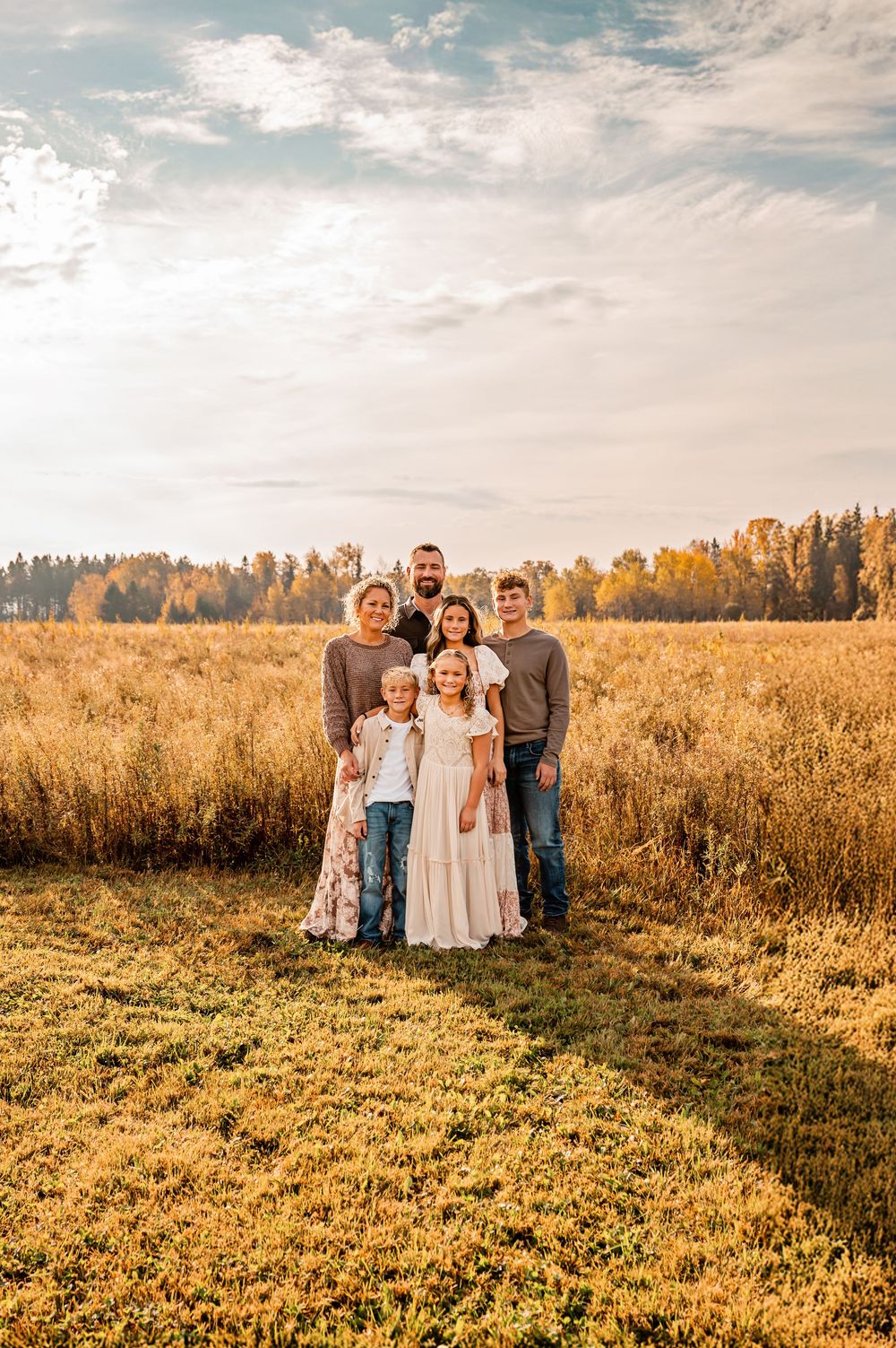 A group stands together in a golden wheat field at sunset with autumn trees in the background.