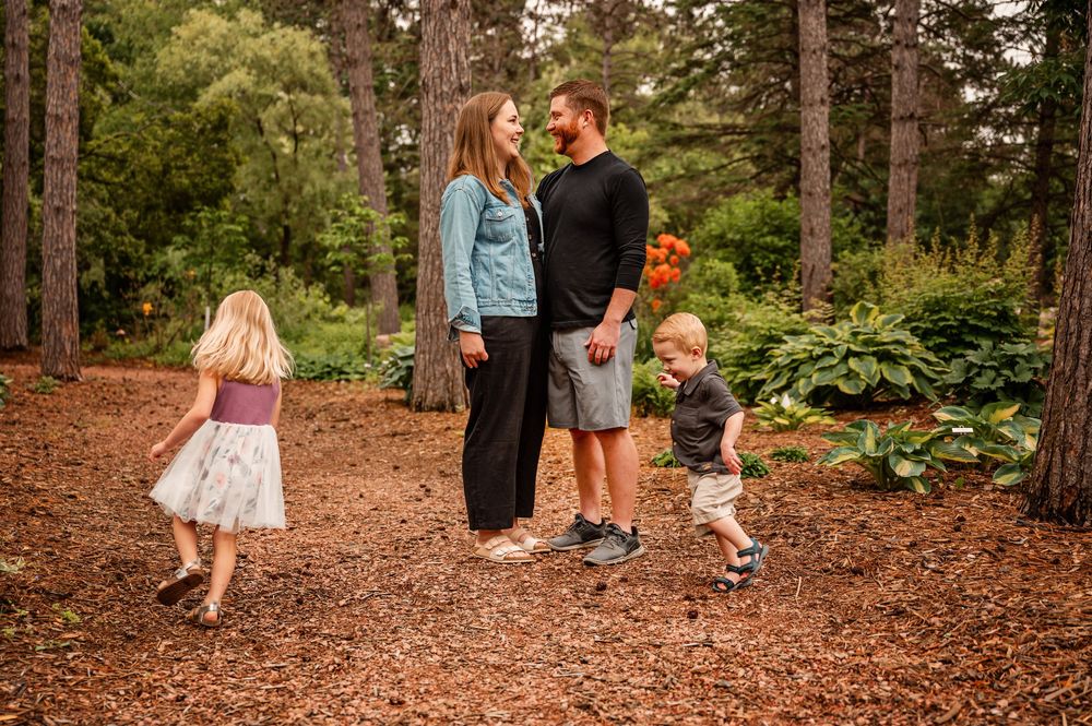 Family members walk together on a winding path through a wooded forest area during an autumn day.