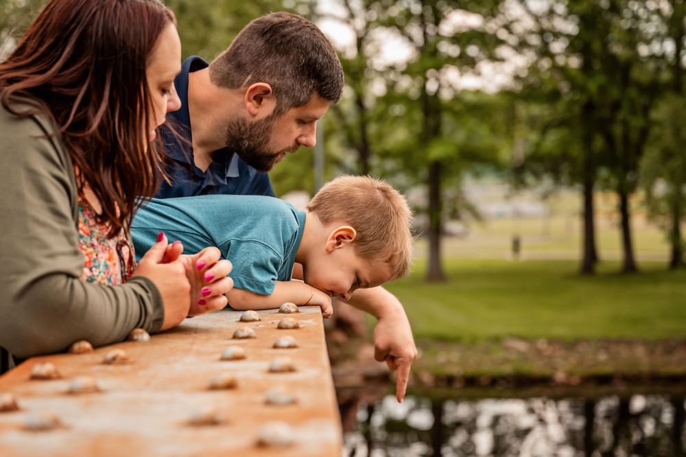 A family plays a board game together at a wooden picnic table in a park setting.