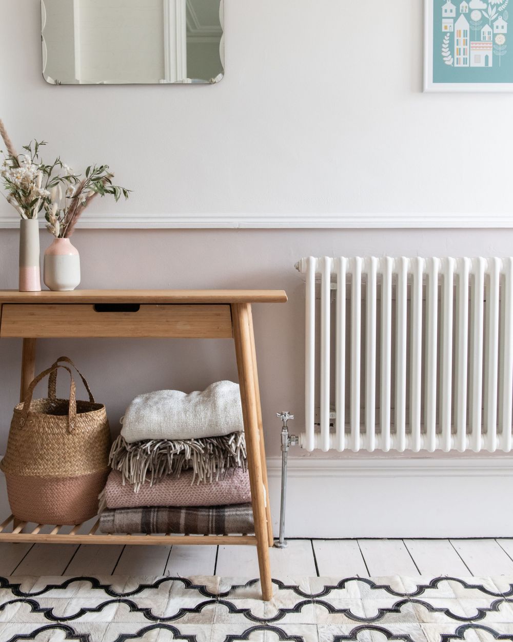 Modern entryway with white radiator, wooden bench, woven baskets and black and white geometric pattern floor tiles.