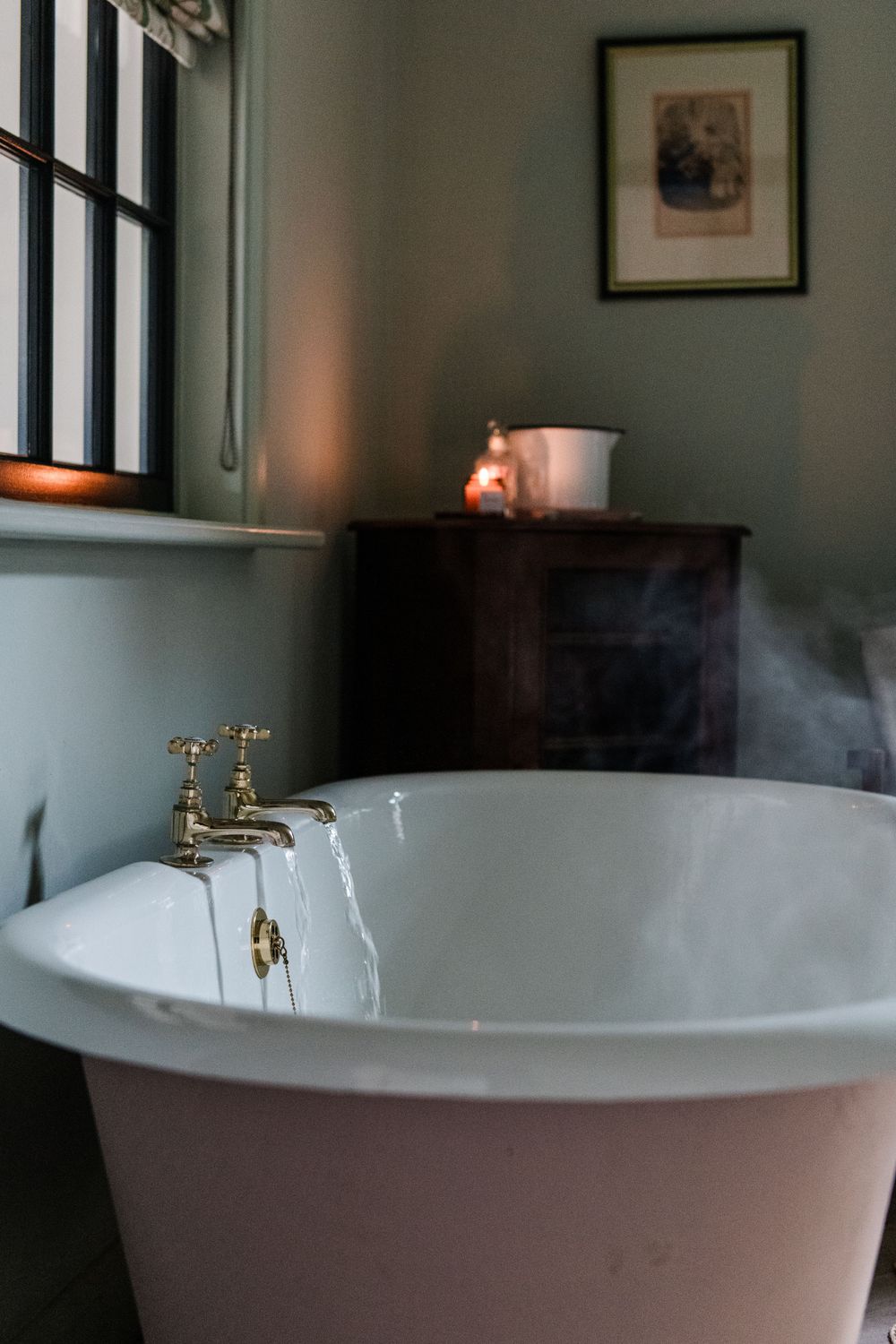 A vintage white clawfoot bathtub with brass fixtures sits in a dimly lit bathroom corner.