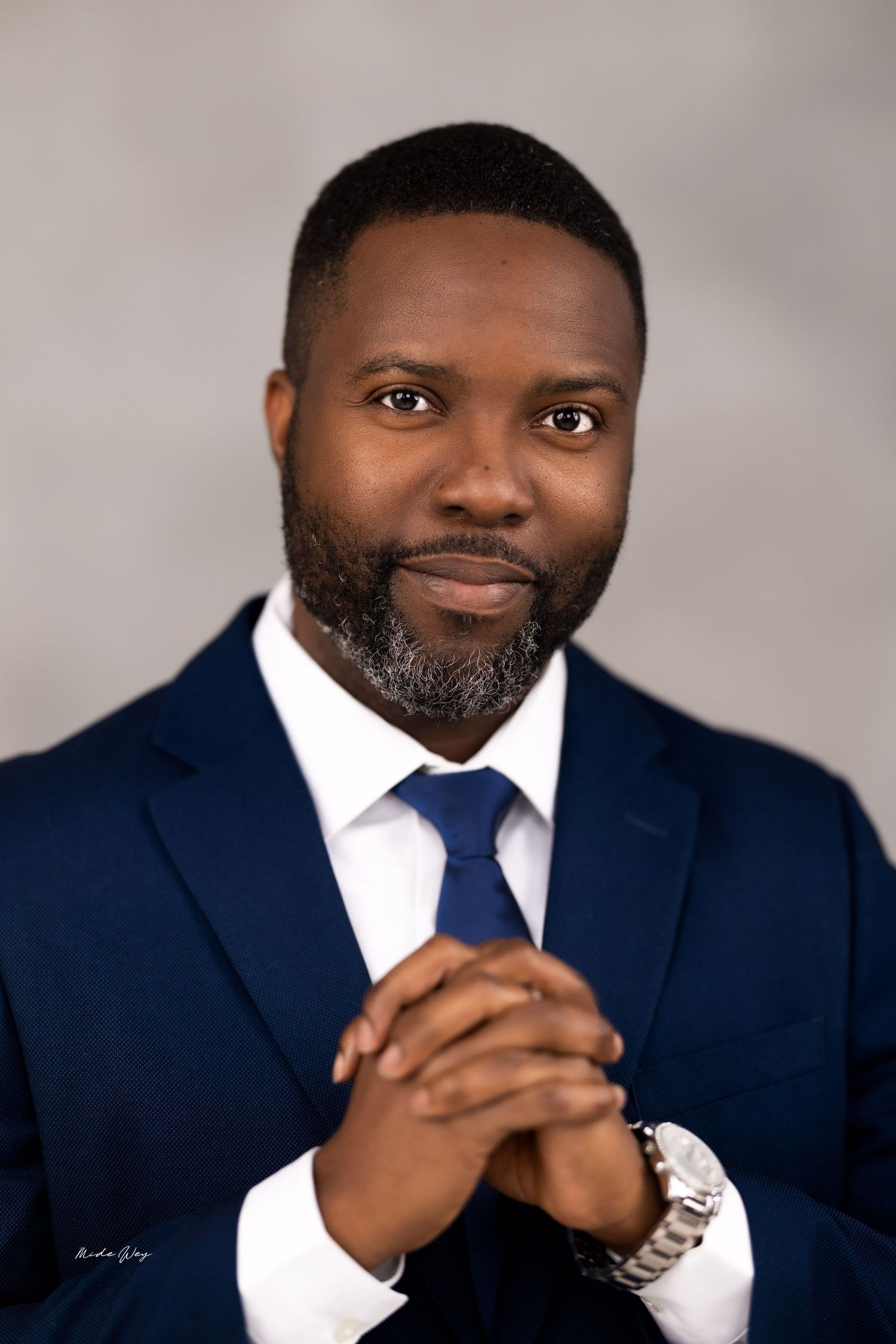 Professional headshot series showing a person in a navy suit and white shirt against a neutral backdrop.