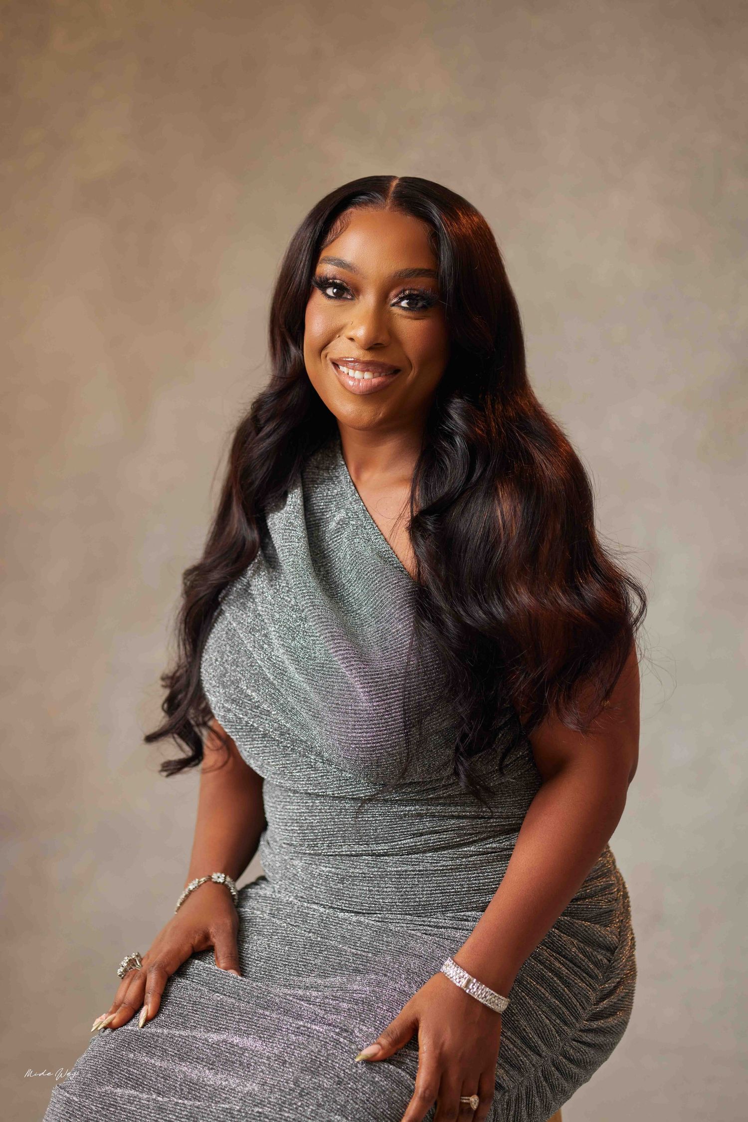 Professional studio portrait featuring a person in a shimmering silver dress with long wavy dark hair and jewelry.