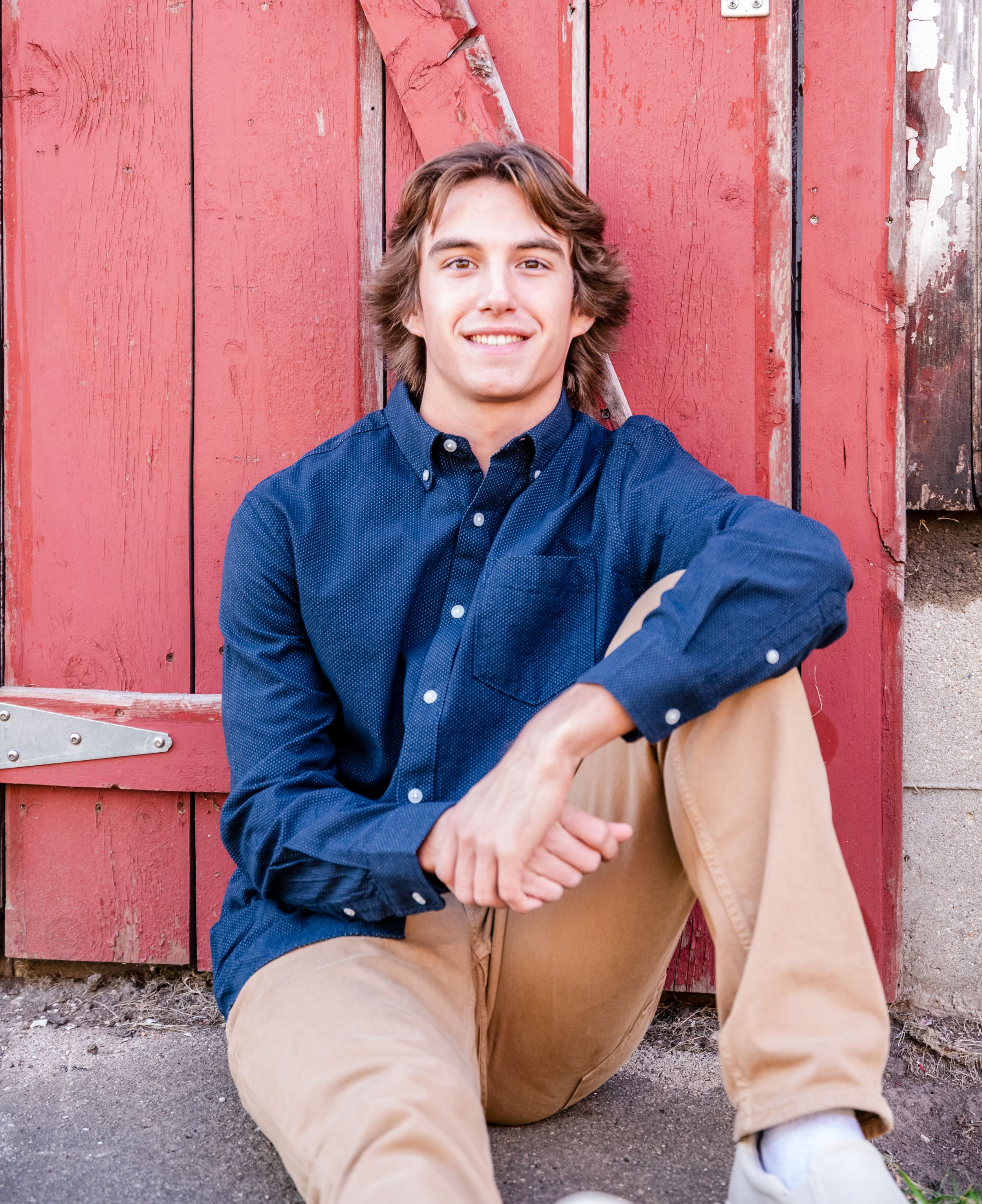 Casual portrait against a red barn door wearing a navy button-down shirt and khaki pants.