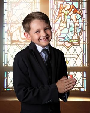 Young boy in black suit jacket poses in front of stained glass windows in a series of expressive shots.