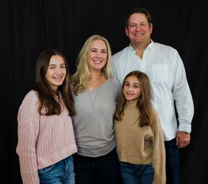 A family of four wearing casual sweaters poses together against a dark background for a portrait studio photograph.