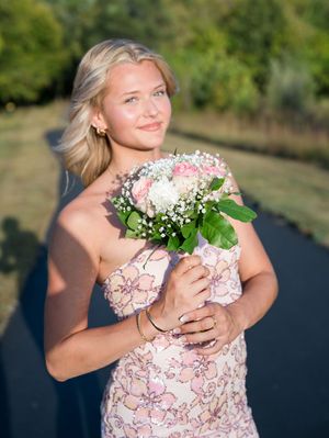 A person in a floral pink dress holds a bouquet of white flowers in an outdoor garden setting.