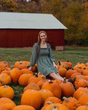 Autumn scene with bright orange pumpkins scattered in front of a rustic red barn surrounded by fall foliage.