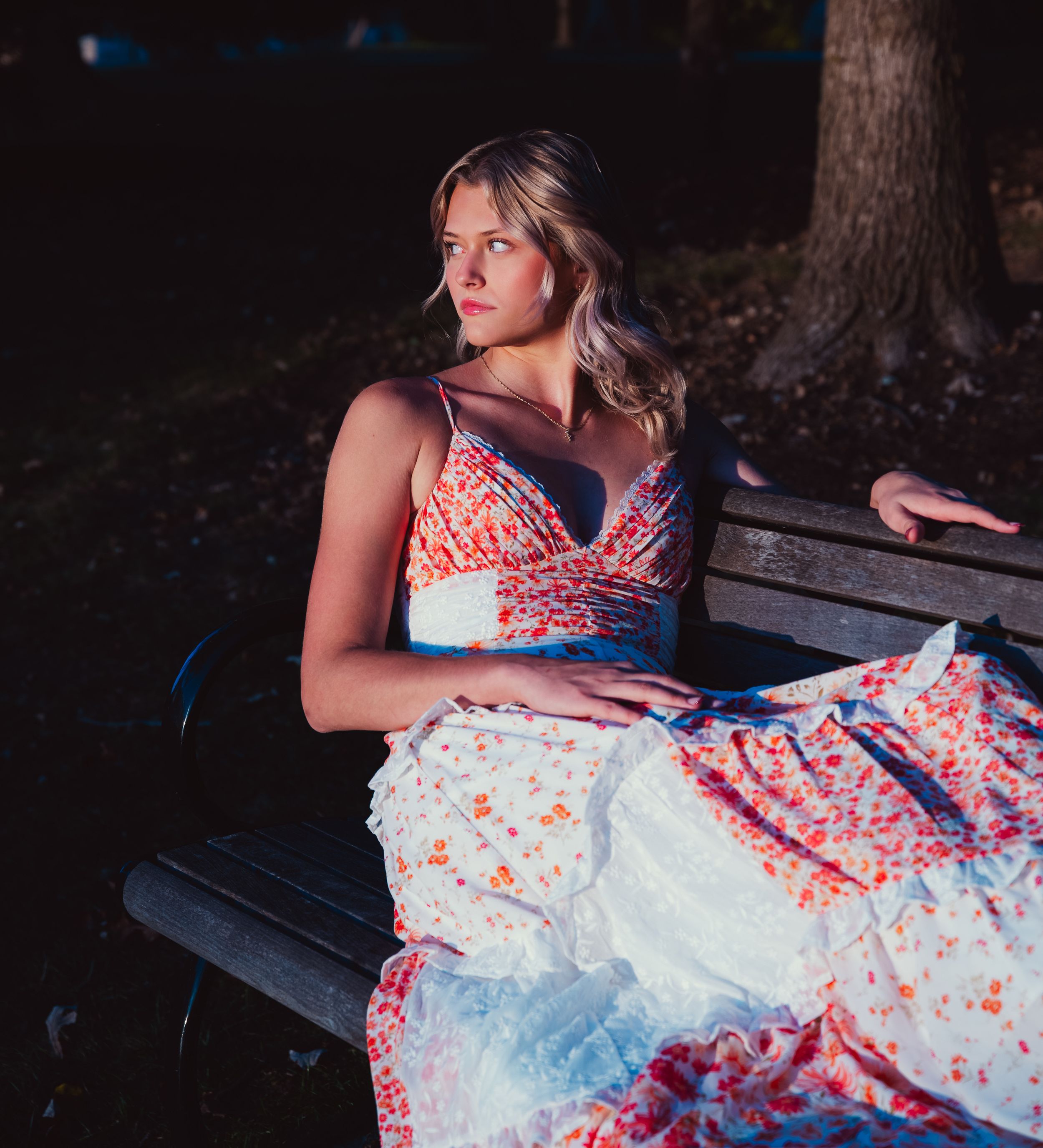 A person in a white and coral dress sits on a dark bench in a dramatic outdoor setting at night.