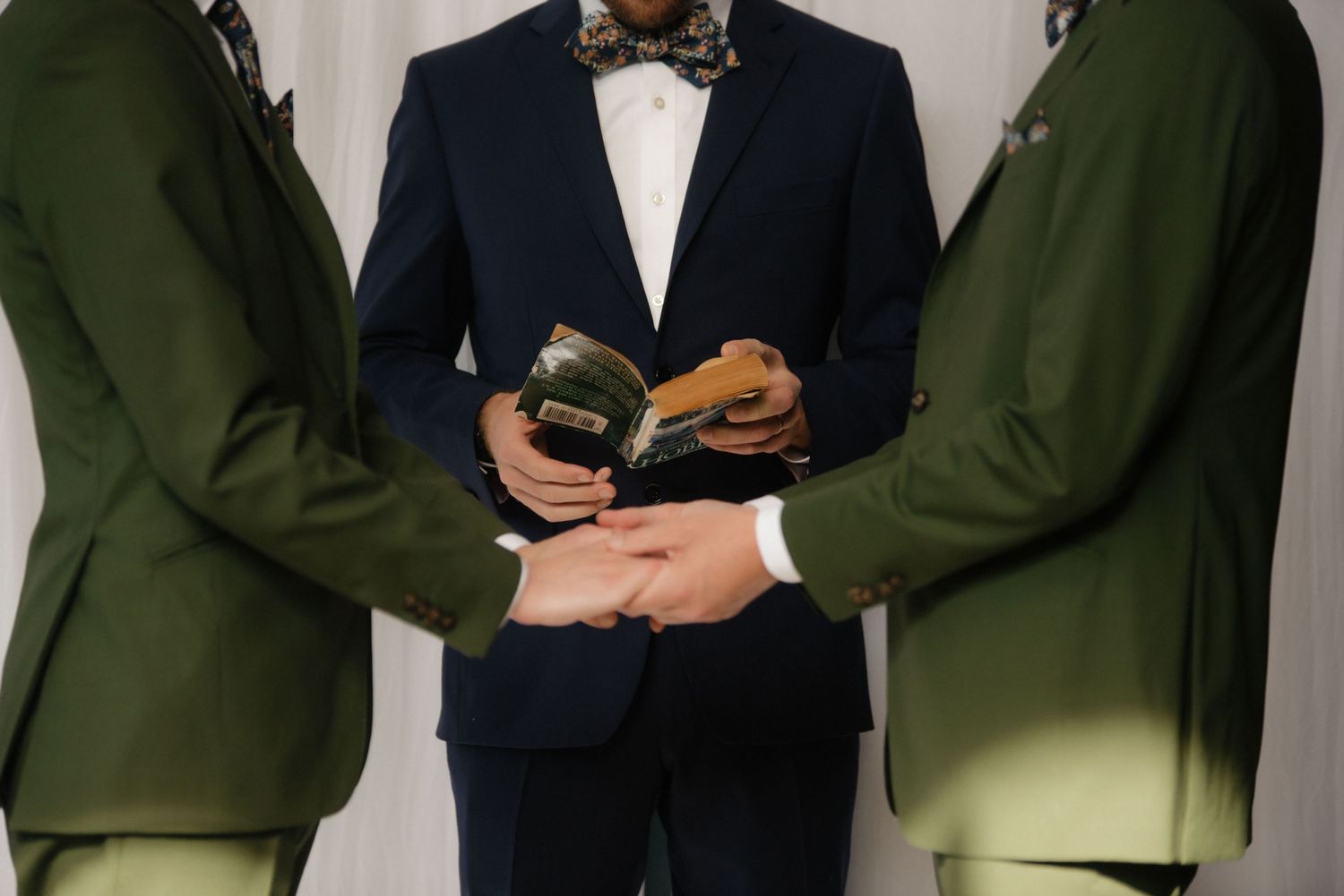 Three people in formal attire, with center figure in navy suit and bowtie.