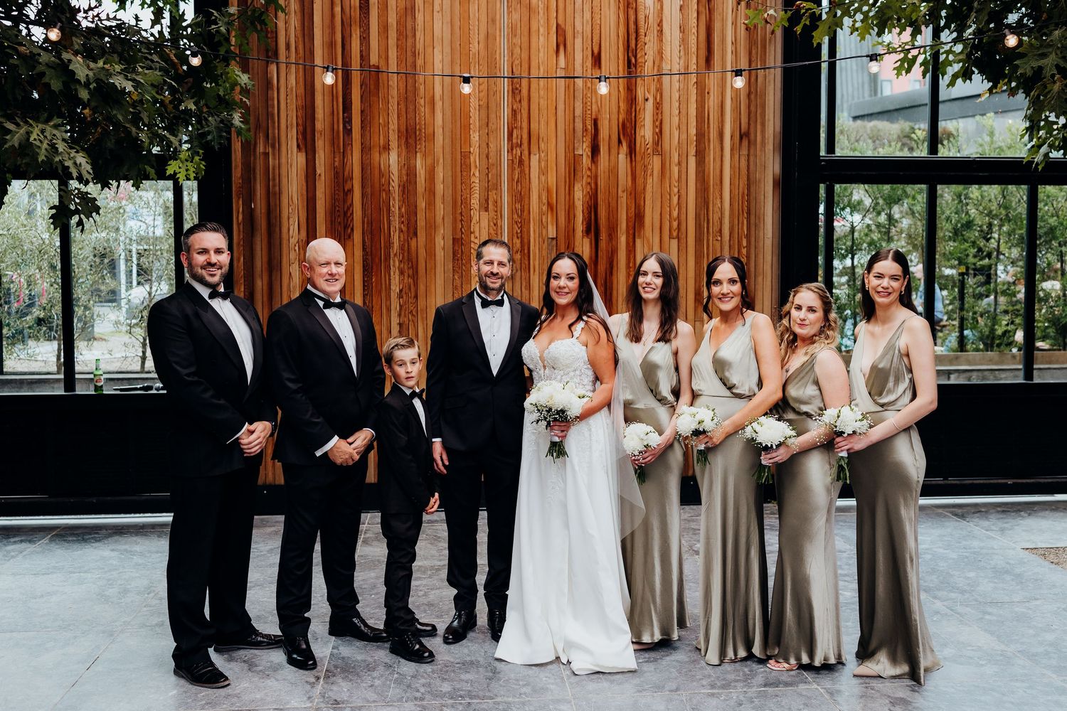 Wedding party in navy blue and teal dresses poses together on white gravel path outdoors.
