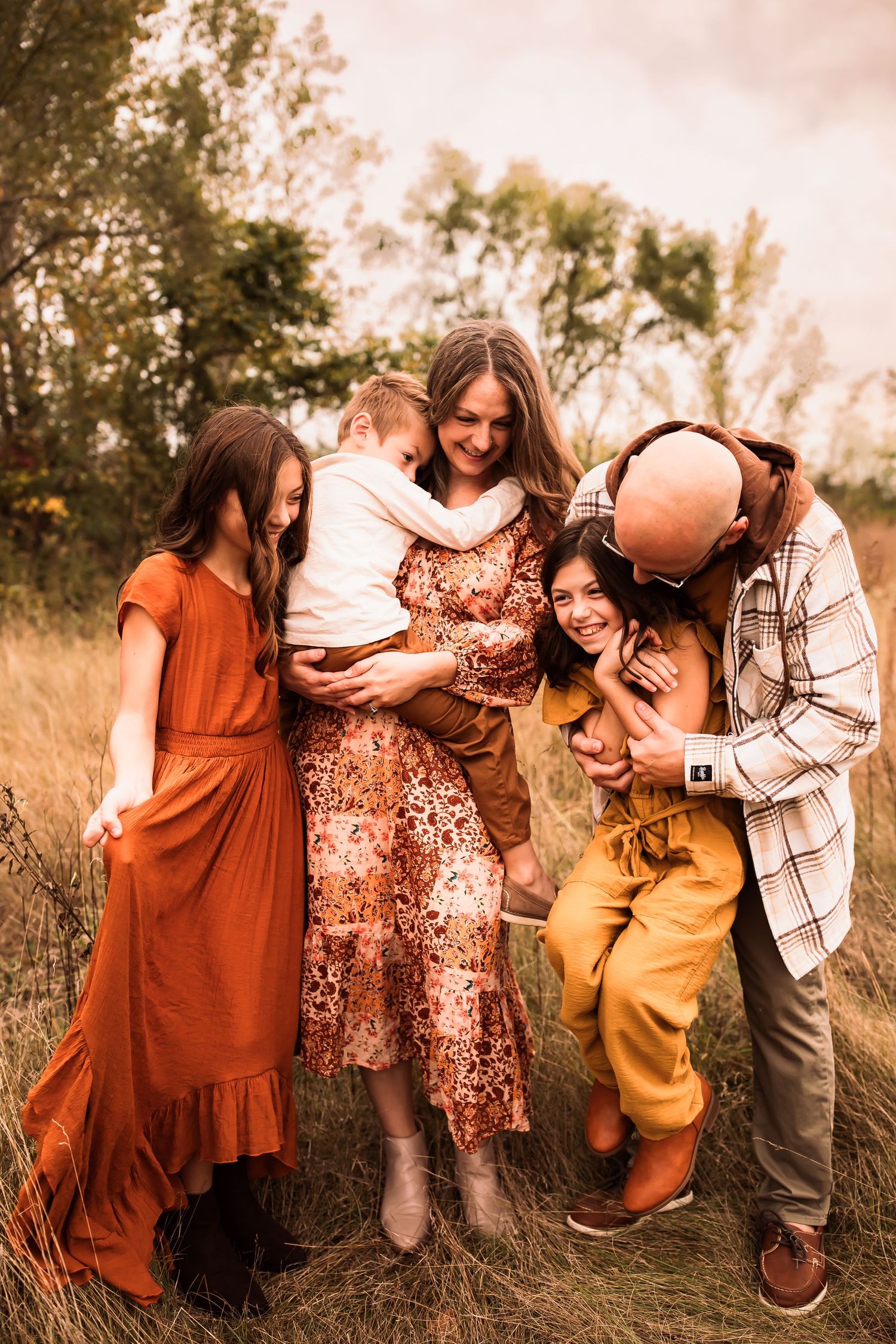 A family dressed in warm earth tones shares a candid moment together in a sun-drenched field at golden hour.