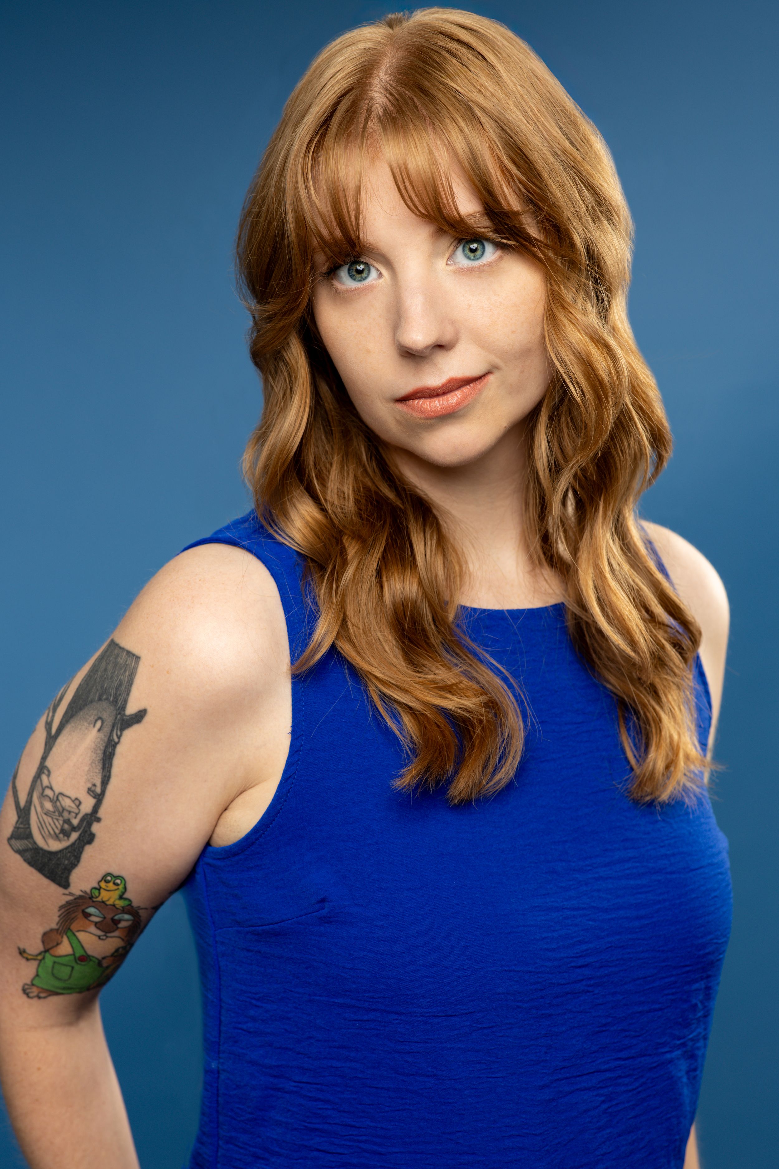 A headshot of a red-headed woman wearing a blue shirt against a blue background. Twin cities headshots. Theatre headshots. Headshots.