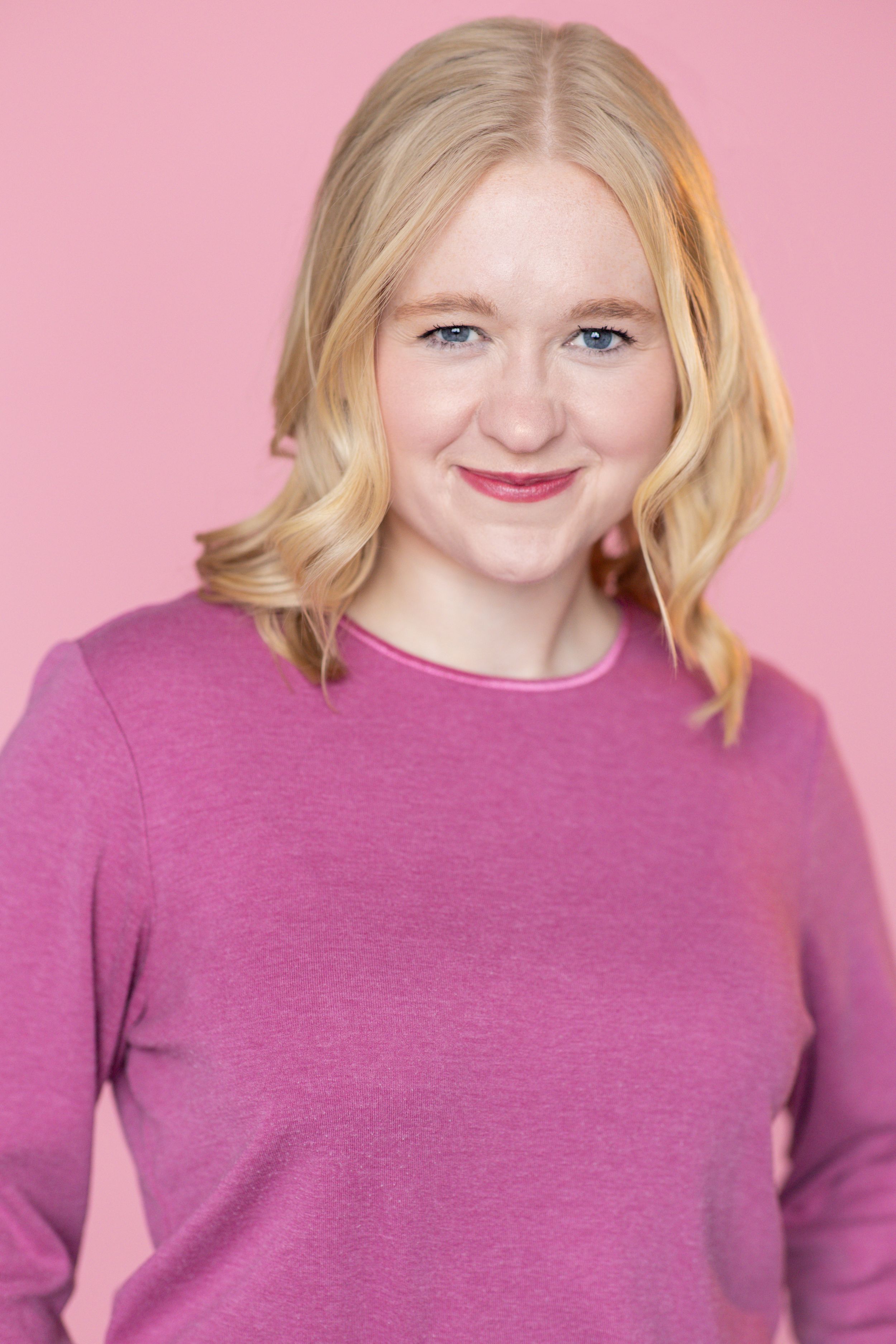 A headshot of a blonde woman wearing a pink sweater against a pink background. Twin cities headshots. Theatre headshots. Headshots.