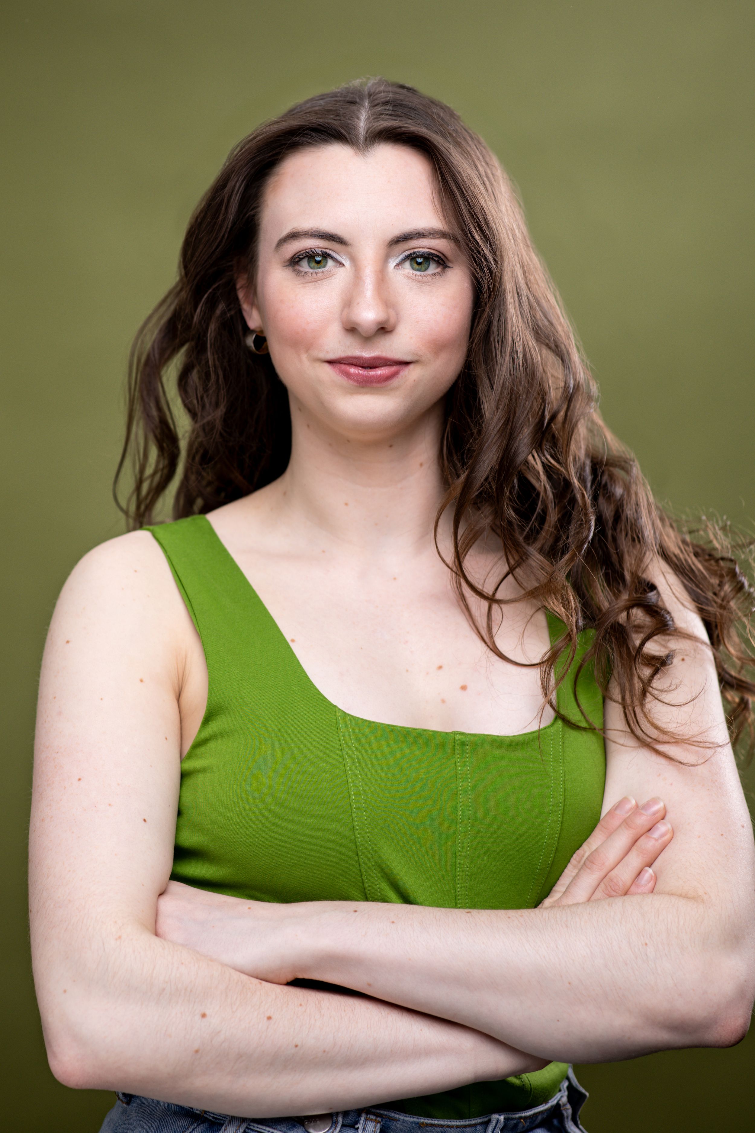 A headshot of a brunette woman wearing a green shirt against a green background. Twin cities headshots. Theatre headshots. Headshots.