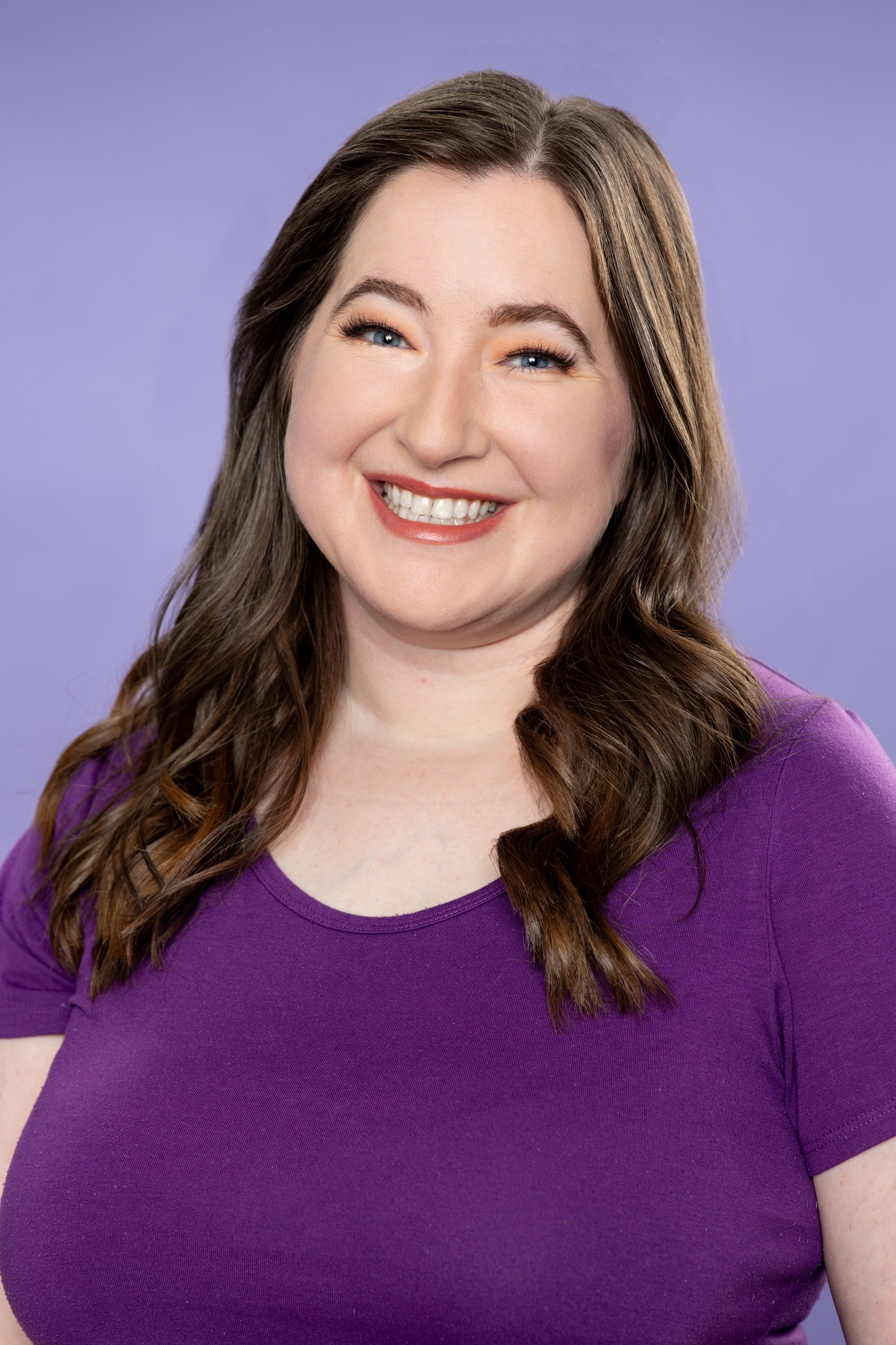 A headshot of a brunette woman wearing a purple shirt against a purple background. Twin cities headshots. Theatre headshots. Headshots.