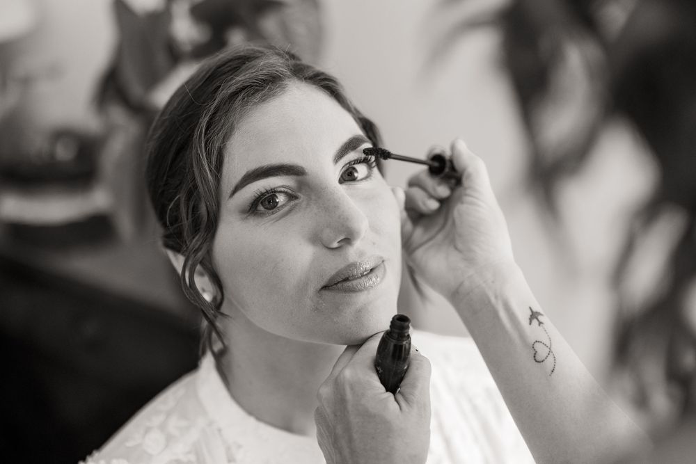 Black and white portrait of a bride having mascara applied by a makeup artist while getting ready for her wedding day.