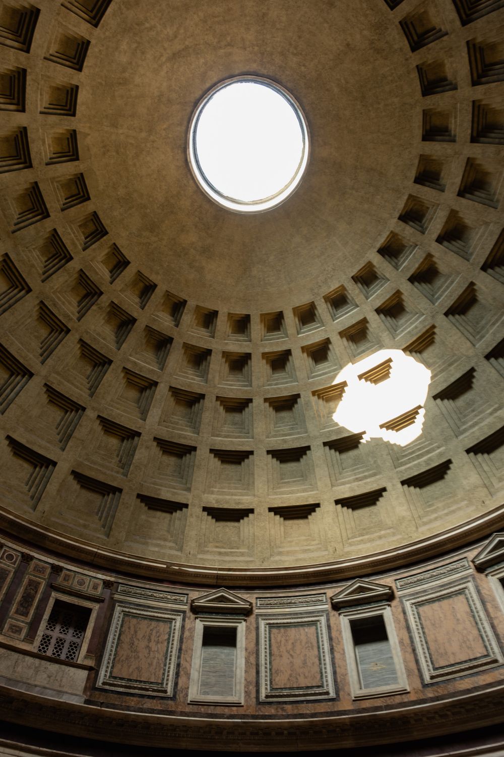 Sunlight streams through the oculus of the Pantheon dome in Rome, illuminating the coffered ceiling.
