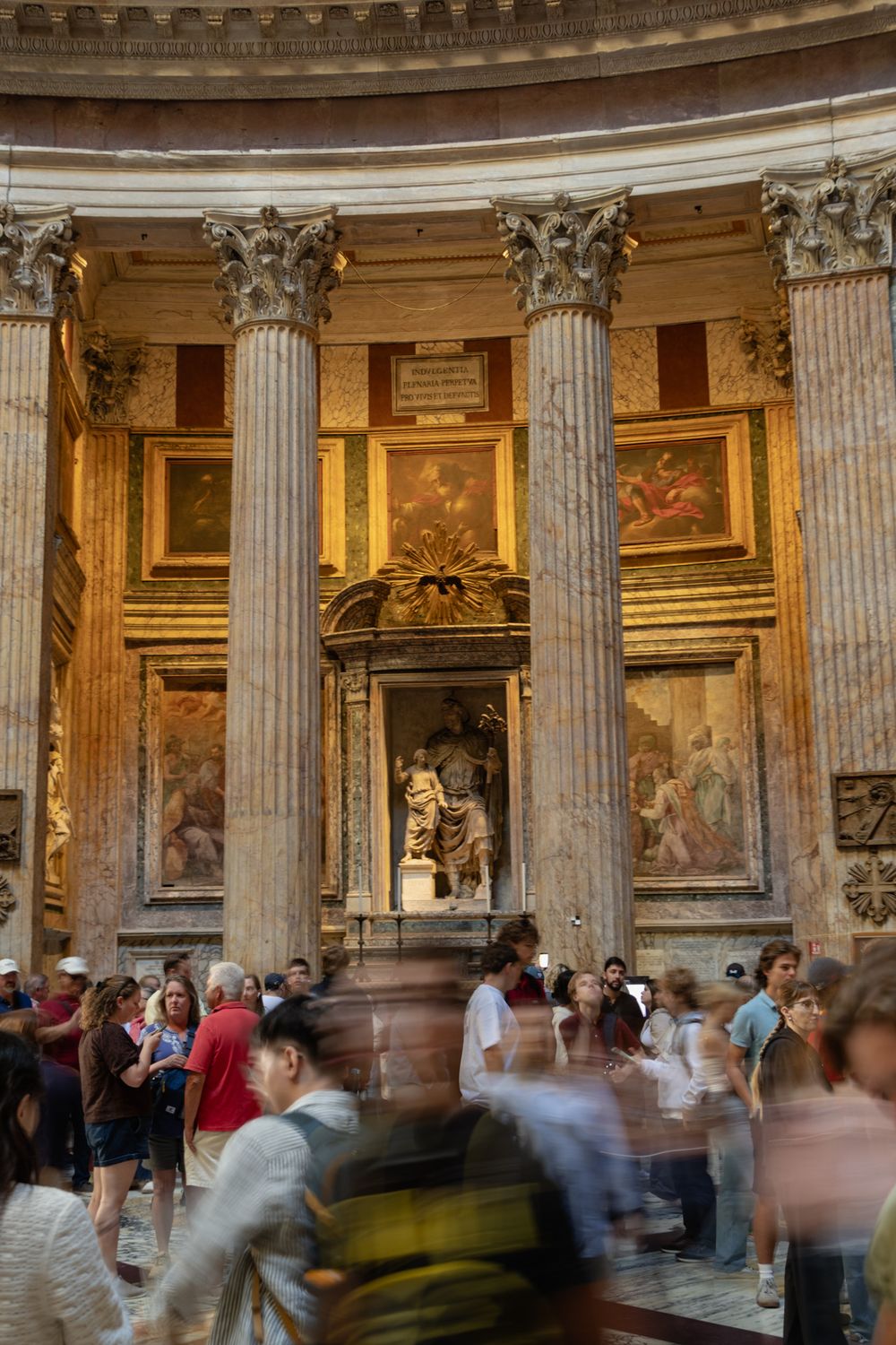 Tourists crowd past Corinthian columns and an ornate altar with frescoes inside the Pantheon in Rome, Italy.